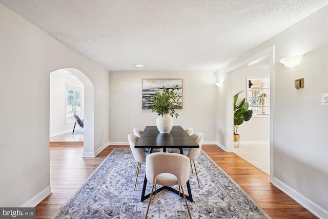 dining area with arched walkways, a textured ceiling, baseboards, and wood finished floors