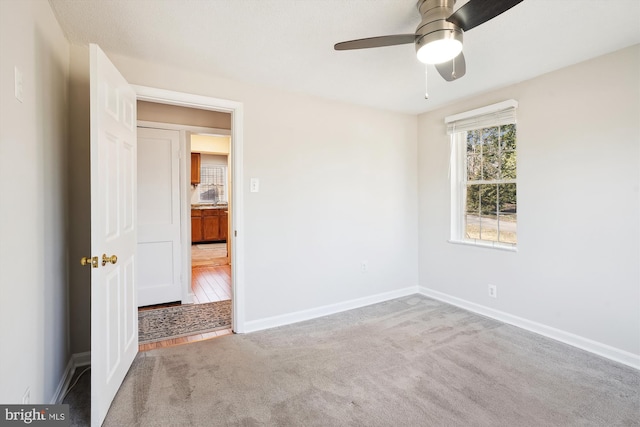 carpeted spare room with a ceiling fan and baseboards