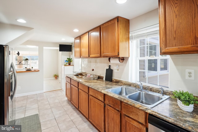 kitchen featuring light tile patterned floors, tasteful backsplash, appliances with stainless steel finishes, brown cabinets, and a sink