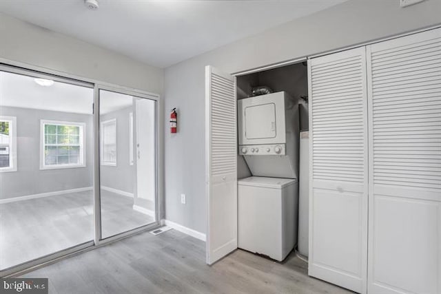 laundry room featuring stacked washer / drying machine and light wood-type flooring