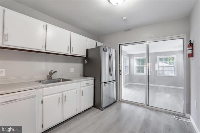 kitchen featuring sink, white cabinets, dishwasher, light hardwood / wood-style flooring, and stainless steel refrigerator