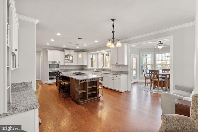 kitchen with light stone counters, ceiling fan with notable chandelier, sink, white cabinets, and a kitchen island