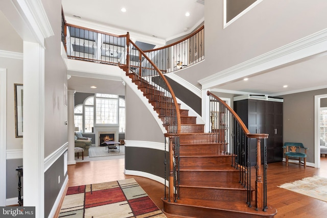 stairs featuring a towering ceiling, wood-type flooring, and ornamental molding