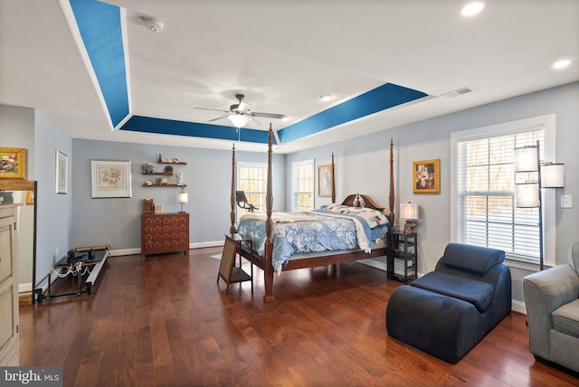 bedroom featuring ceiling fan, dark hardwood / wood-style flooring, a raised ceiling, and multiple windows