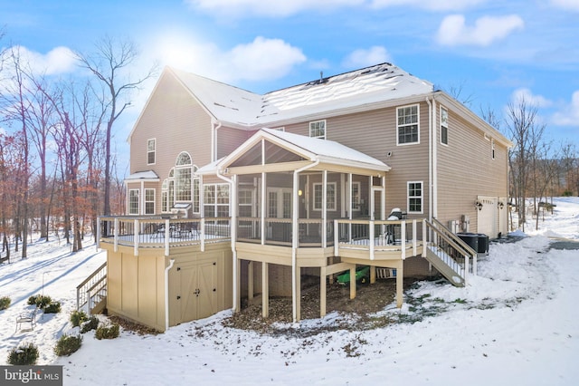 snow covered house with a sunroom, central air condition unit, and a wooden deck