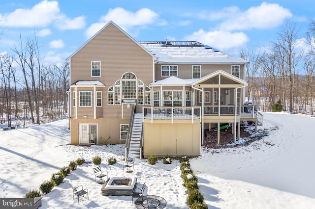 snow covered property with a sunroom, an outdoor fire pit, and a wooden deck