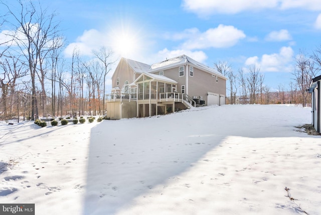 snow covered back of property with a sunroom and a garage