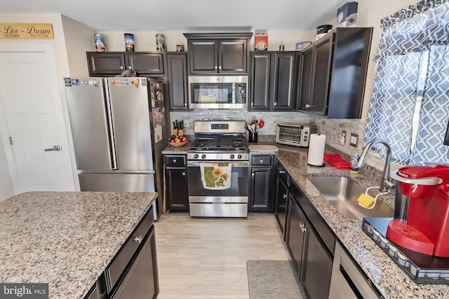 kitchen featuring backsplash, light stone counters, stainless steel appliances, sink, and light hardwood / wood-style floors