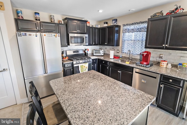 kitchen with tasteful backsplash, light stone counters, stainless steel appliances, sink, and a center island