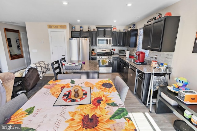 kitchen featuring a center island, light stone counters, light hardwood / wood-style flooring, decorative backsplash, and appliances with stainless steel finishes