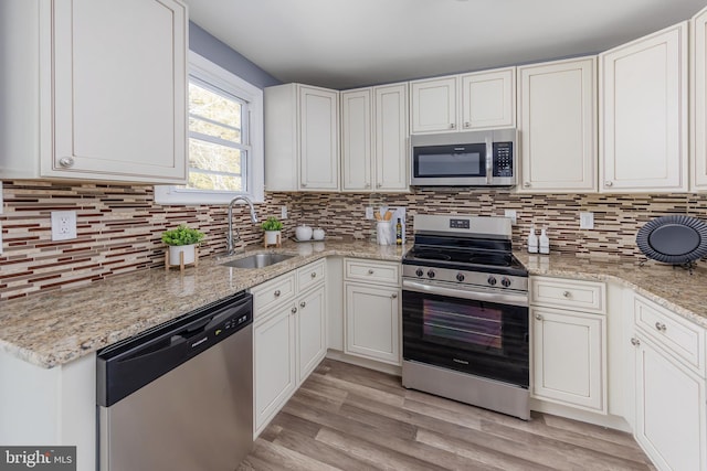 kitchen with appliances with stainless steel finishes, light stone counters, white cabinetry, and sink