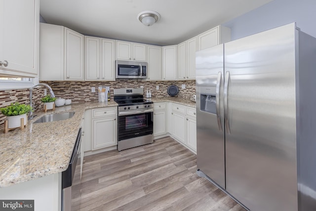 kitchen with sink, appliances with stainless steel finishes, light hardwood / wood-style floors, light stone counters, and white cabinetry