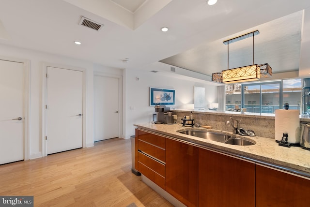 kitchen with light stone countertops, sink, backsplash, pendant lighting, and light hardwood / wood-style floors