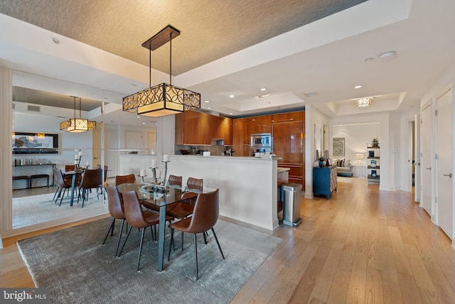 dining space with a tray ceiling and light wood-type flooring