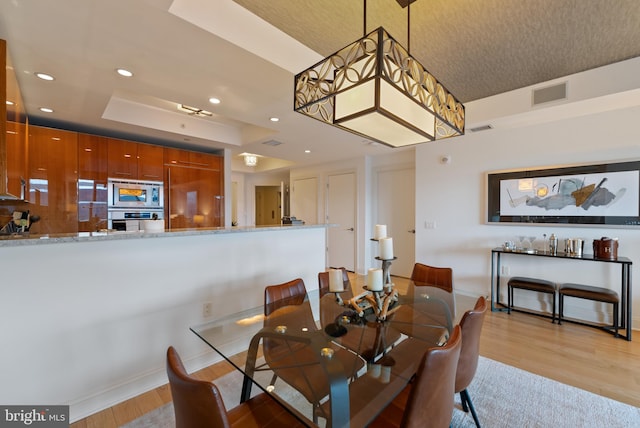 dining area featuring a raised ceiling and light wood-type flooring