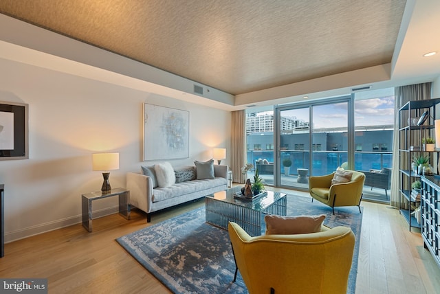 living room featuring hardwood / wood-style floors, a raised ceiling, and a wall of windows