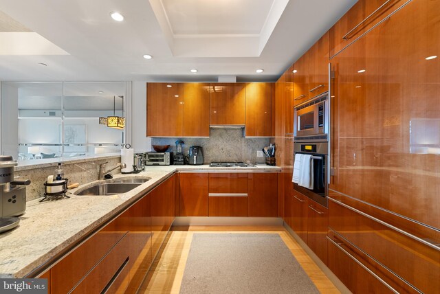 kitchen with light stone counters, a raised ceiling, sink, built in appliances, and hanging light fixtures