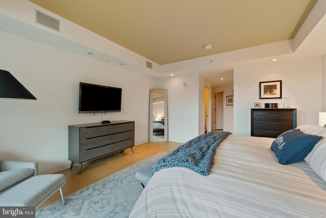 bedroom with light hardwood / wood-style floors and a raised ceiling