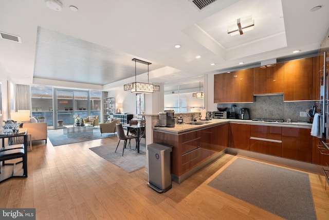 kitchen with light hardwood / wood-style flooring, kitchen peninsula, hanging light fixtures, and a tray ceiling