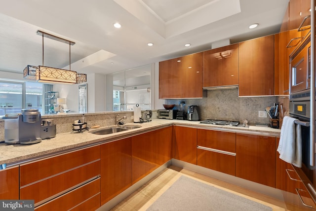 kitchen with decorative backsplash, light stone countertops, light wood-type flooring, sink, and pendant lighting