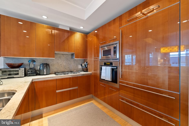 kitchen with backsplash, exhaust hood, sink, built in appliances, and light stone countertops