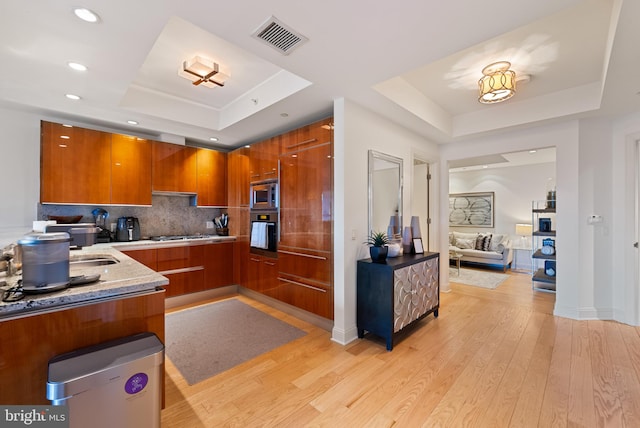 kitchen with stainless steel appliances, a raised ceiling, and light hardwood / wood-style floors