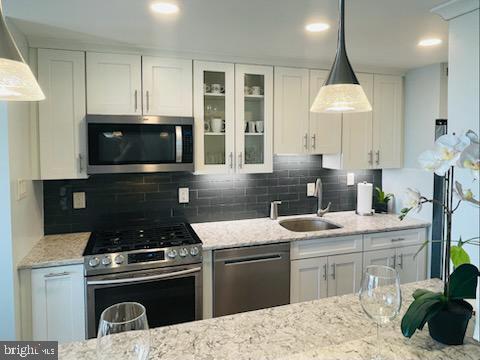 kitchen featuring appliances with stainless steel finishes, backsplash, white cabinetry, and decorative light fixtures