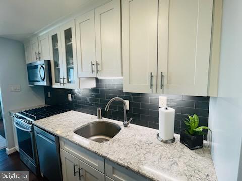 kitchen with decorative backsplash, sink, white cabinetry, light stone countertops, and appliances with stainless steel finishes