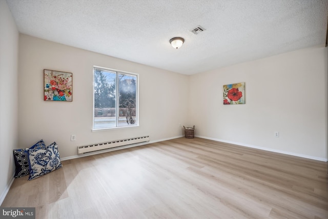 spare room with a textured ceiling, light wood-type flooring, a baseboard radiator, and visible vents