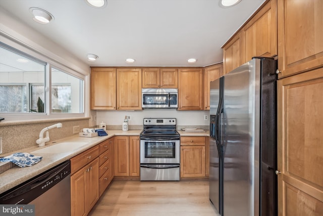 kitchen with a sink, light wood-style floors, stainless steel appliances, and light countertops