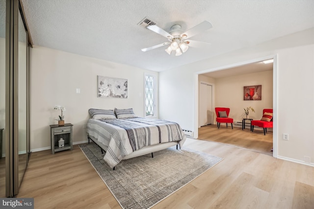 bedroom with a baseboard heating unit, visible vents, light wood-style flooring, and a textured ceiling