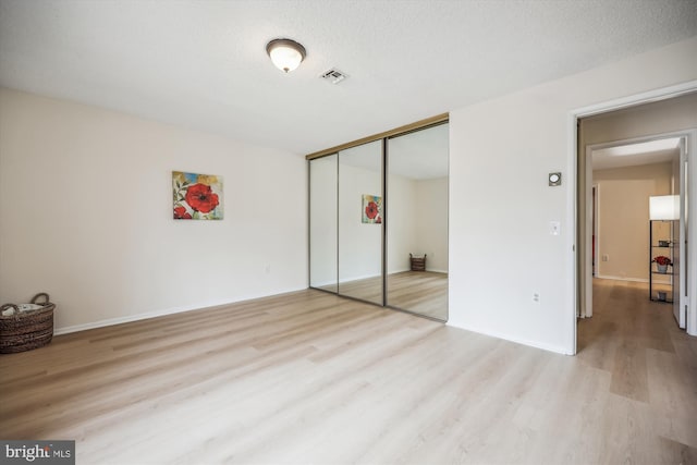 unfurnished bedroom with light wood-style floors, a closet, visible vents, and a textured ceiling