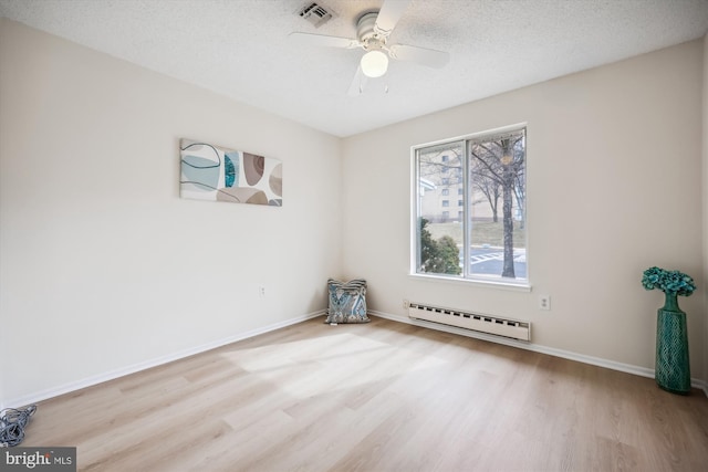 unfurnished room featuring baseboards, visible vents, light wood-style flooring, baseboard heating, and a textured ceiling