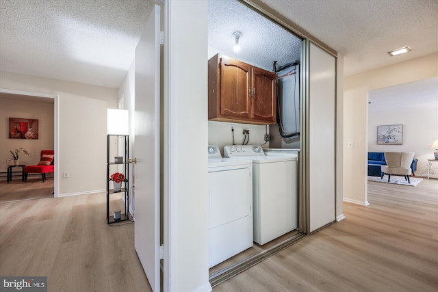 laundry room featuring cabinet space, baseboards, a textured ceiling, washer and dryer, and light wood-style floors