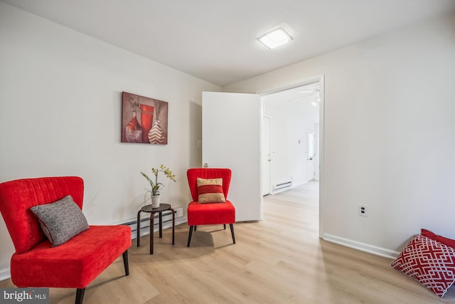 sitting room with a baseboard radiator, light wood-style flooring, and baseboards