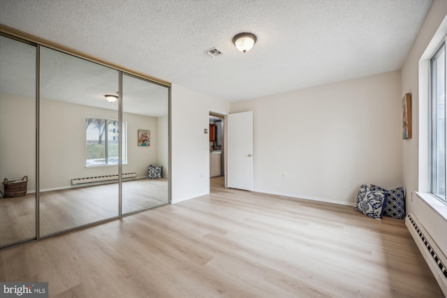 unfurnished bedroom with light wood-style floors, a baseboard radiator, visible vents, and a closet