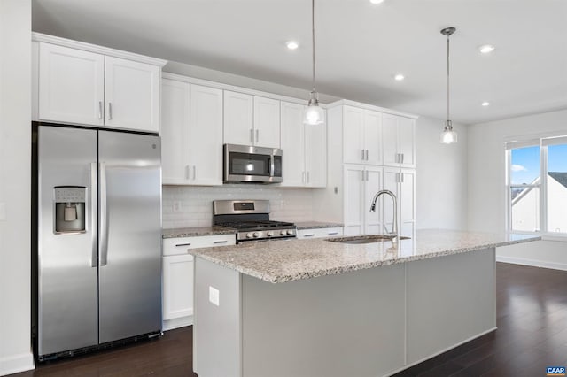 kitchen with stainless steel appliances, sink, decorative light fixtures, white cabinetry, and a center island with sink