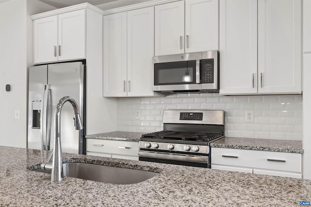 kitchen featuring light stone counters, stainless steel appliances, decorative backsplash, white cabinetry, and sink