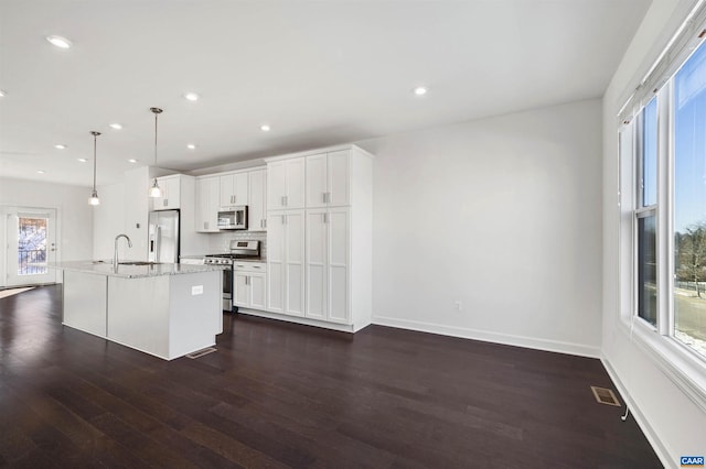 kitchen featuring dark wood-type flooring, decorative light fixtures, stainless steel appliances, an island with sink, and white cabinetry