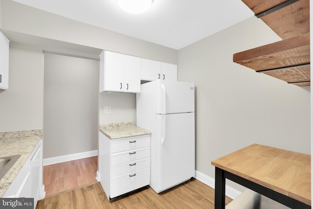 kitchen with light hardwood / wood-style floors, white fridge, light stone countertops, and white cabinetry