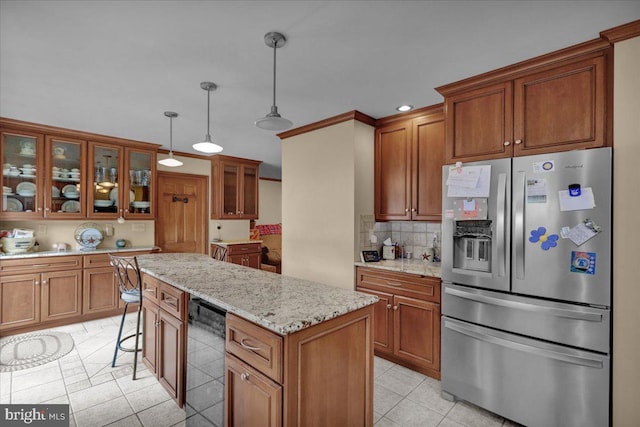 kitchen with light stone countertops, stainless steel refrigerator with ice dispenser, a kitchen island, wine cooler, and hanging light fixtures