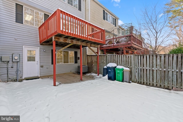 snow covered back of property with cooling unit and a wooden deck