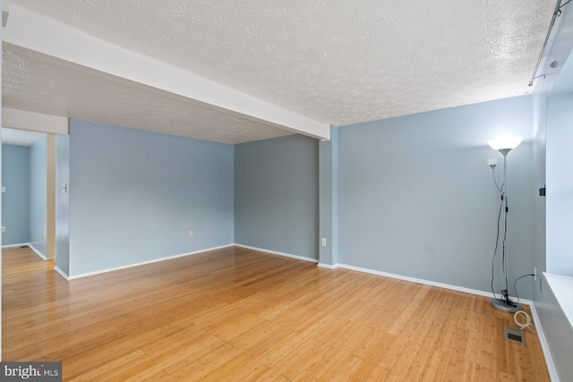 spare room featuring beamed ceiling, a textured ceiling, and light hardwood / wood-style flooring