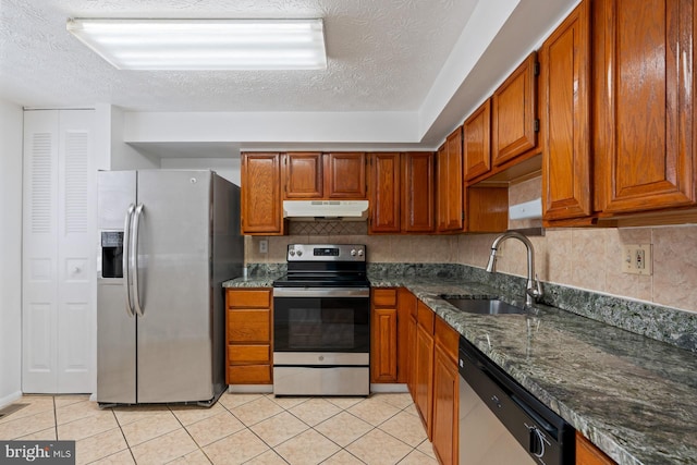 kitchen featuring sink, light tile patterned floors, dark stone counters, and appliances with stainless steel finishes