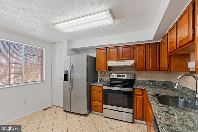 kitchen with light tile patterned floors, sink, appliances with stainless steel finishes, and dark stone counters