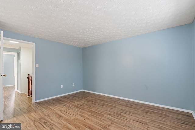 spare room with a textured ceiling and light hardwood / wood-style flooring