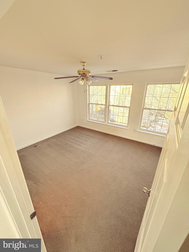 empty room featuring ceiling fan, a wealth of natural light, and dark carpet