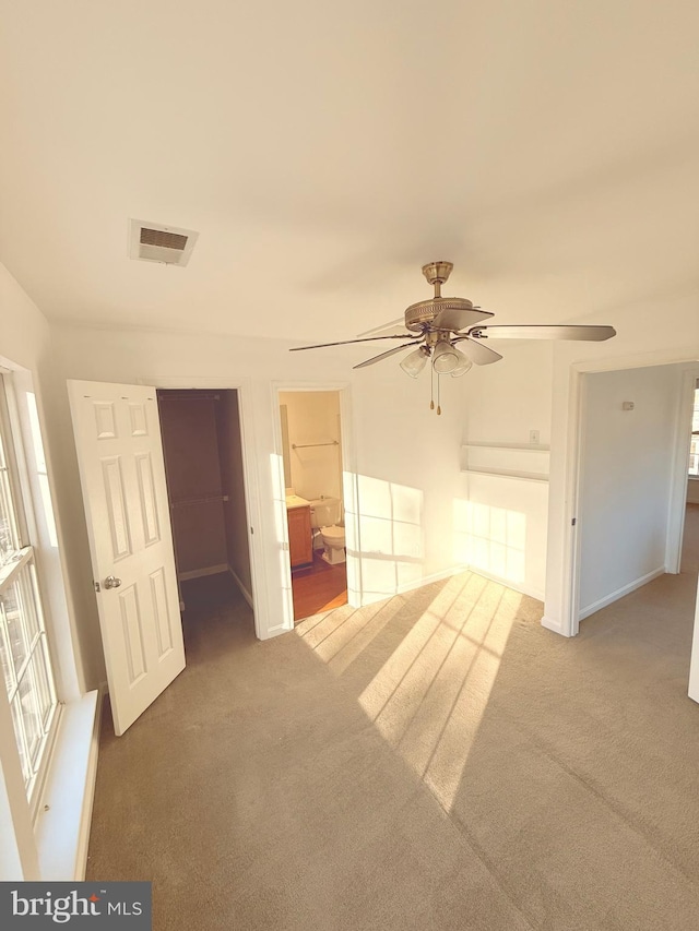 unfurnished bedroom with ensuite bathroom, ceiling fan, carpet, and multiple windows