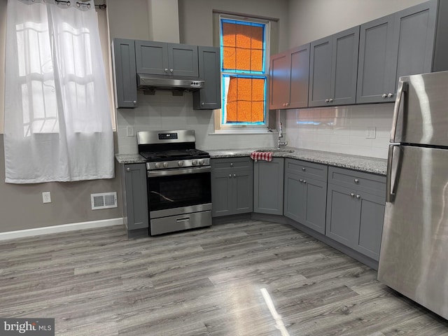 kitchen with light stone counters, gray cabinetry, stainless steel appliances, sink, and light hardwood / wood-style flooring