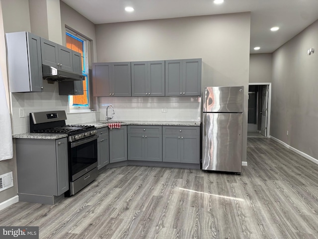 kitchen with stainless steel appliances, light stone counters, gray cabinetry, and sink